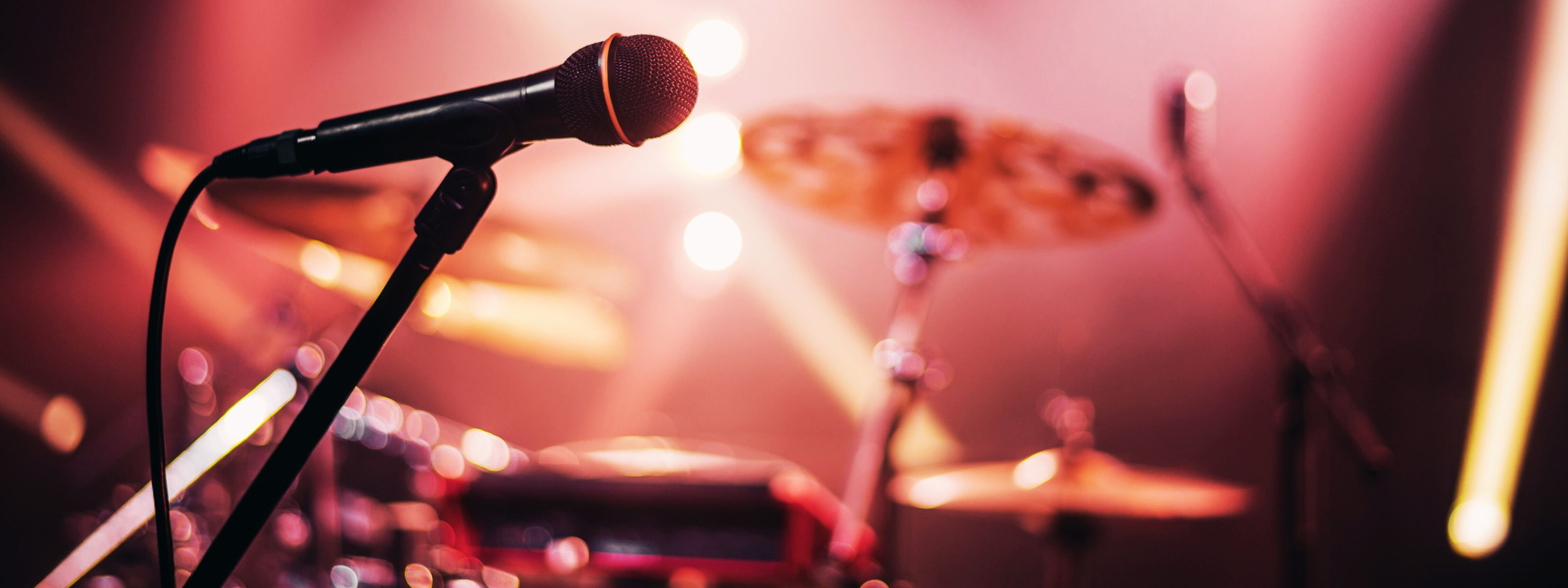 Das Bild zeigt ein Mikrofon auf einer Bühne, im Hintergrund ein Schlagzeug